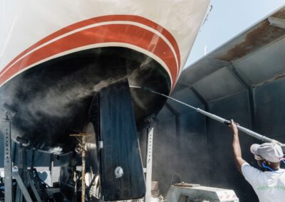 Operaio che lava la carena di una barca con idro-pulitrice in un capannone navale