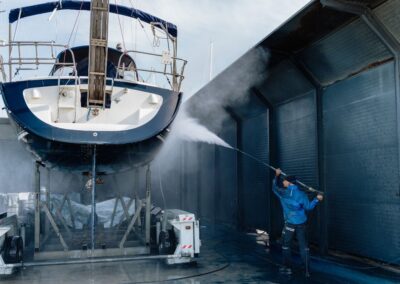 Operaio che lava la carena di una barca con idropulitrice in un capannone navale