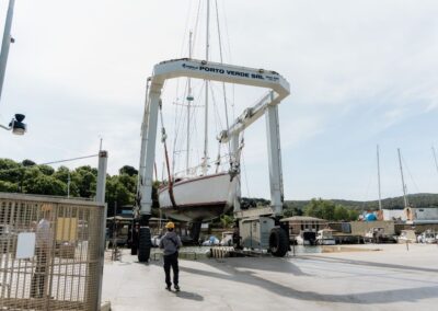 Barca a vela sollevata da una gru mobile nel cantiere navale Porto Verde, con operatori a terra